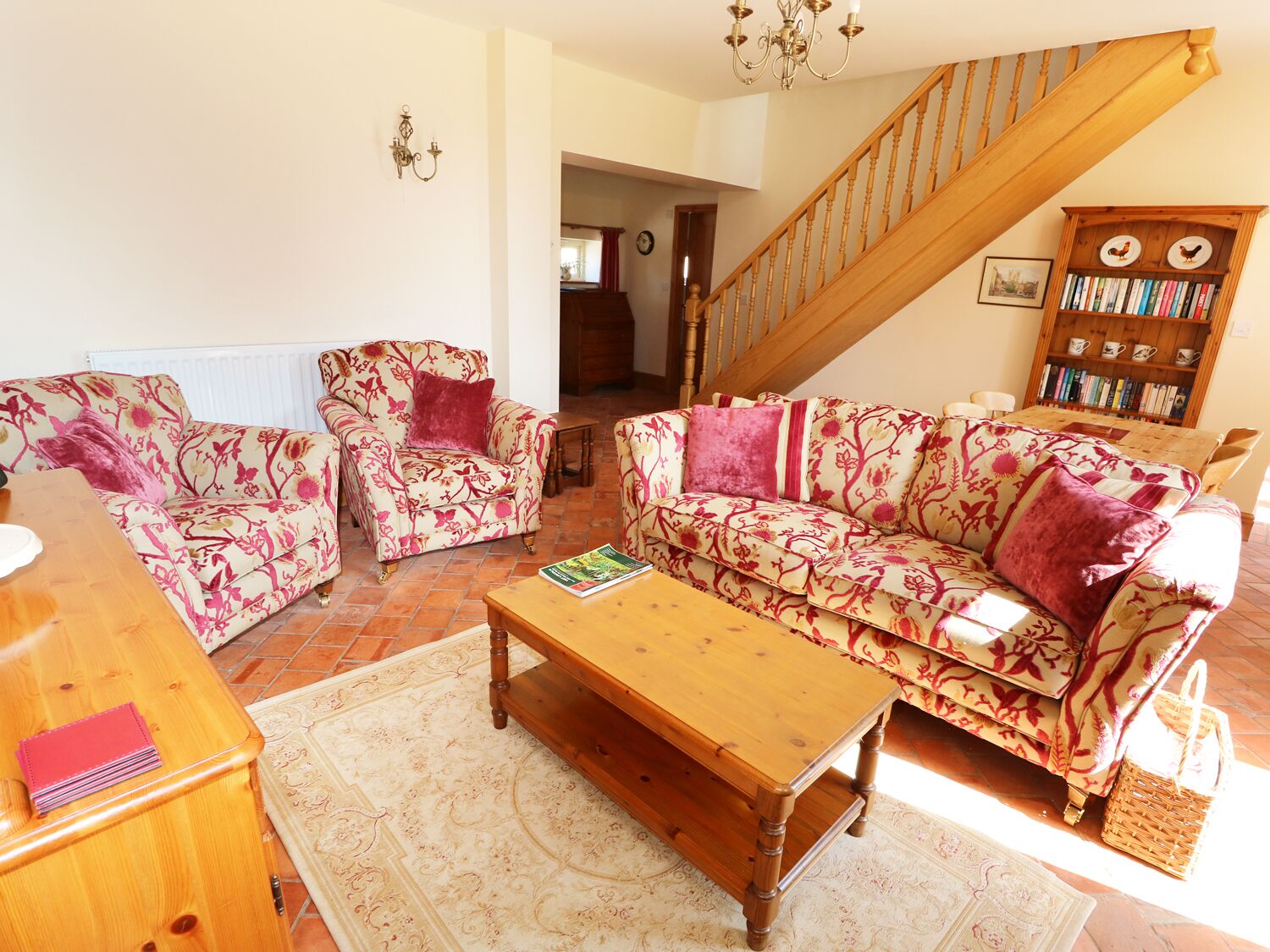 A living room with floral-patterned sofas, a wooden coffee table, and a bookshelf.