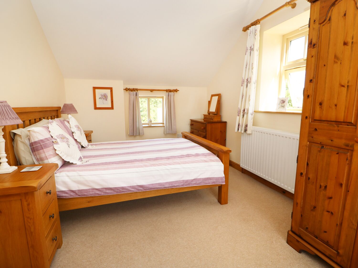 A bedroom with a wooden bed, a nightstand, a dresser, a window with curtains, and a radiator.