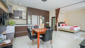 A modern hotel room with a dining area, kitchenette, and a bed with red pillows.