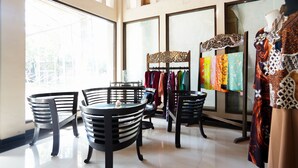 A spacious room with large windows, a central table, and chairs. There are racks of colorful clothing and a mannequin in the background.
