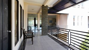 A spacious balcony with a stone pillar, a wooden bench, and a metal railing overlooking a building.