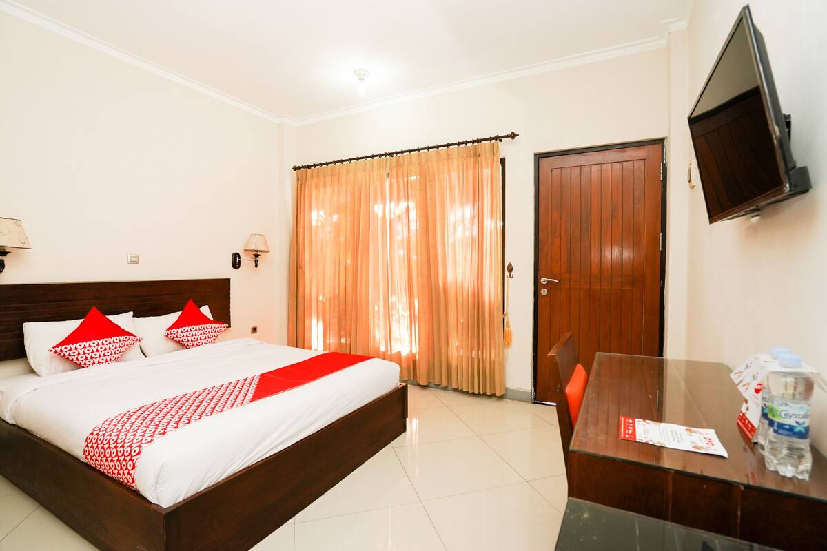A hotel room with a bed, a TV, a desk with a bottle of water, and a door.
