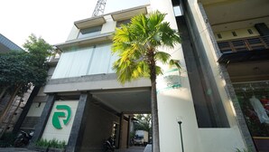 A building with a prominent green logo on the facade, a covered parking area, and a palm tree in the foreground.