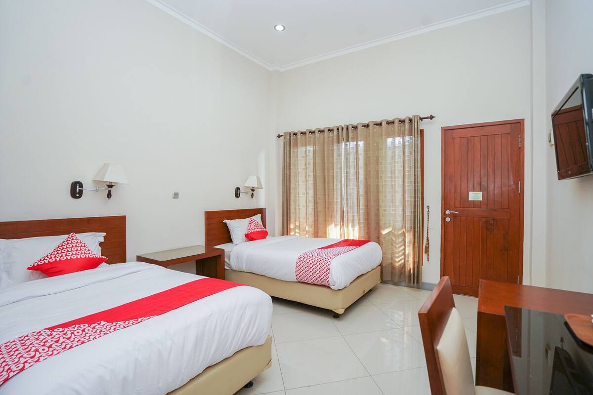 A hotel room with two beds, a wooden door, a TV mounted on the wall, and a dining table with chairs.