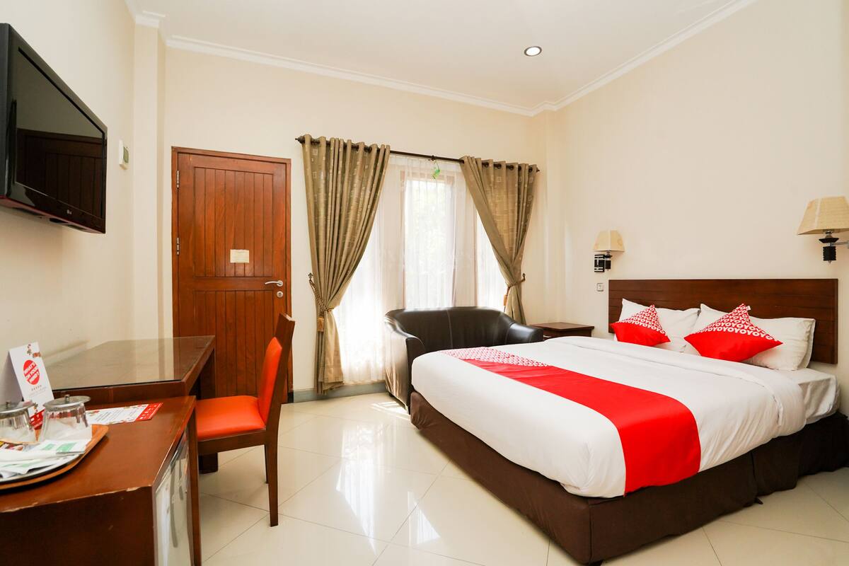 A hotel room with a bed, a desk, a chair, a TV, and curtains.