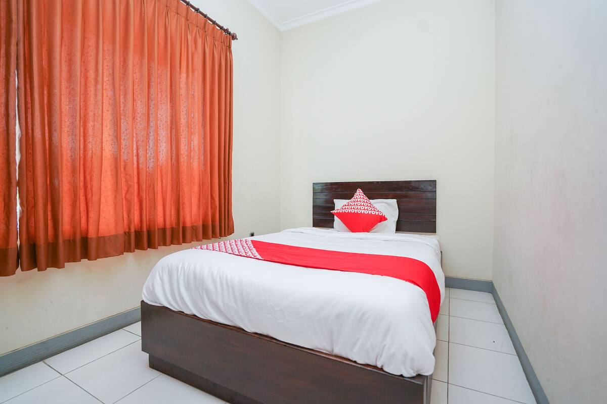 A neatly made bed with white and red bedding, a wooden headboard, and a red curtain.