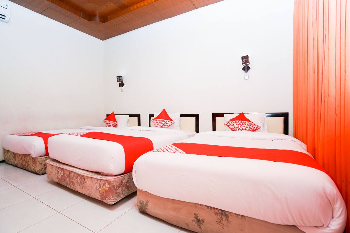 A hotel room with three beds, each with red and white bedding, and a wooden ceiling.