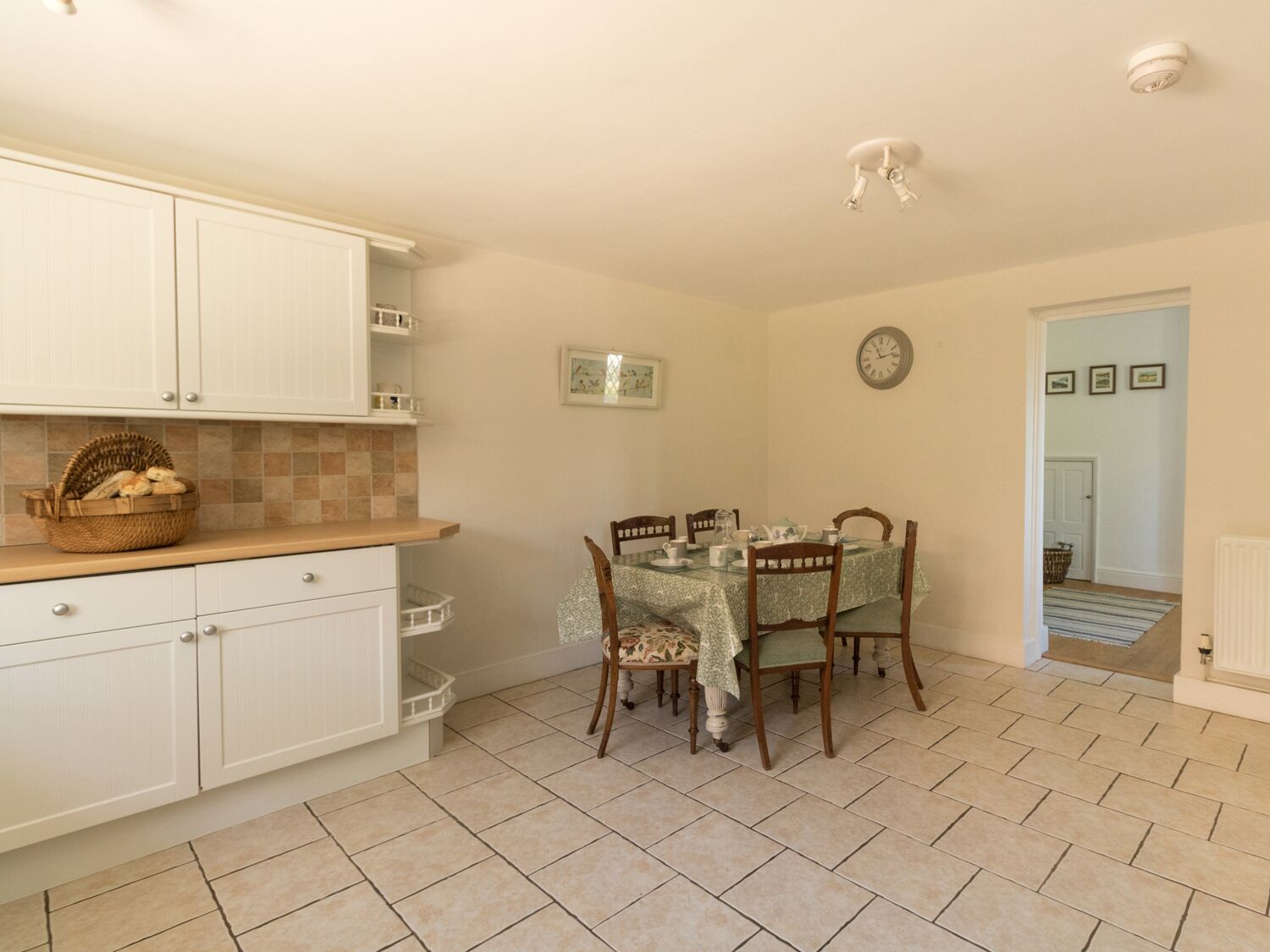 A kitchen with white cabinets, a dining table with chairs, and a clock on the wall.