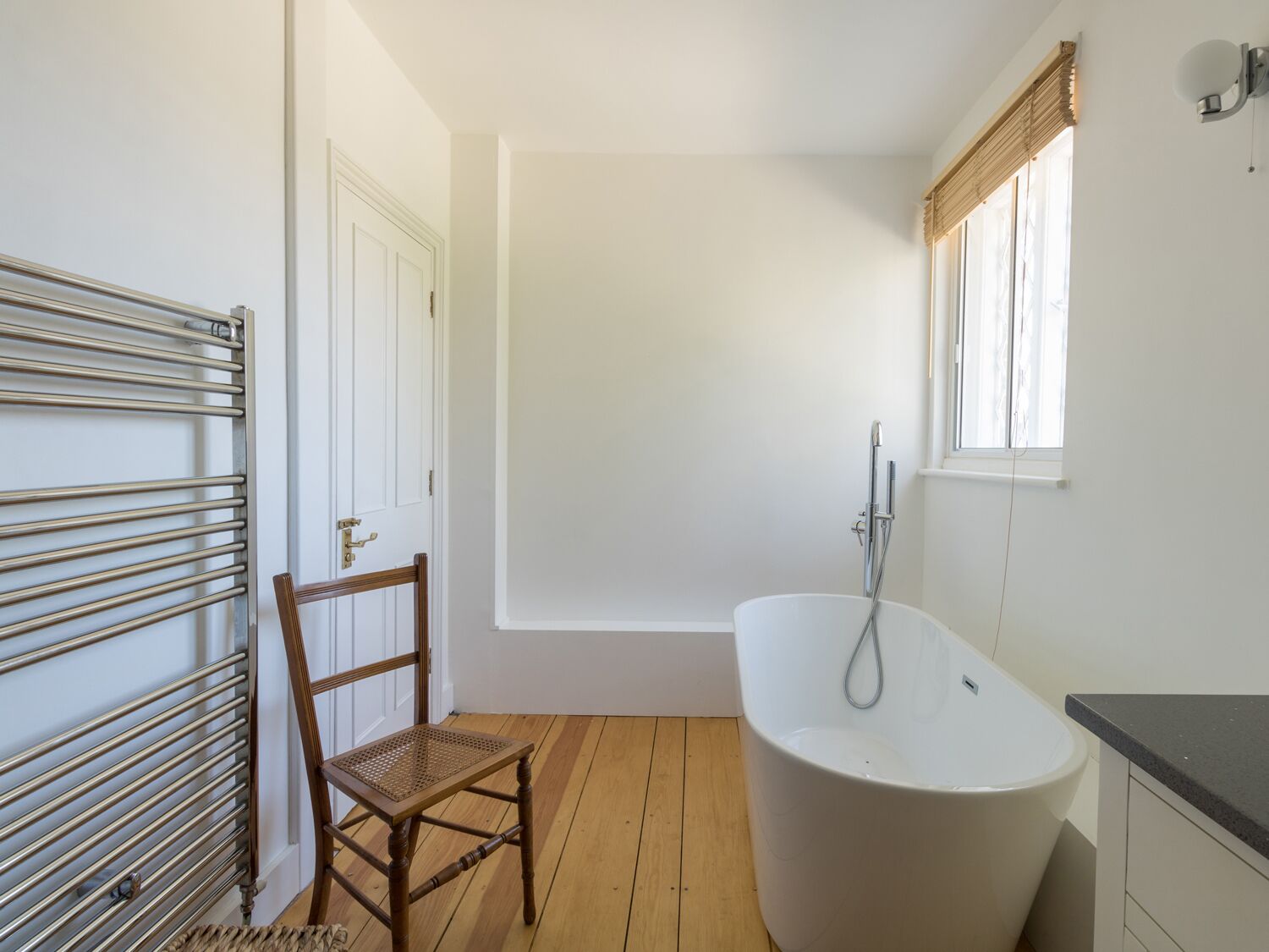 Un baño con una bañera independiente, una silla de madera, un radiador y una ventana con persianas.
