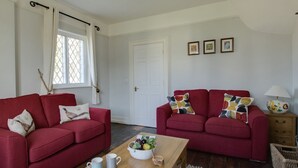 A living room with two red sofas, a wooden coffee table with a fruit bowl, and a white door. - The Old School House (Dorchester)