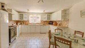 A spacious kitchen with white cabinets, a central island, and a dining area with a table and chairs. - The Old School House (Dorchester)