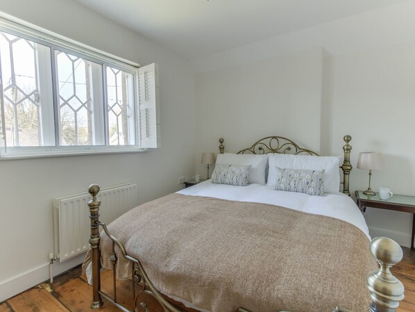 A bedroom with a bed, a radiator, a window with shutters, and a nightstand with a lamp.