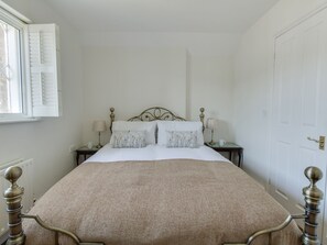 Un dormitorio ordenado con una cama, dos mesitas de noche y una ventana con contraventanas.