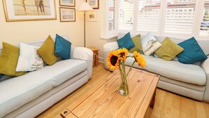 A living room with two light grey sofas, a wooden coffee table, and a vase of sunflowers. There are framed pictures on the wall and a floor lamp. - 32 Cranleigh Close (Bournemouth)