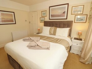 A neatly made bed with towels, a headboard, and bedside lamps.