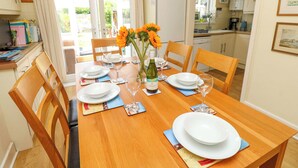 A dining area with a wooden table set for four, surrounded by chairs. A vase with sunflowers and a bottle of wine are on the table. - 32 Cranleigh Close (Bournemouth)