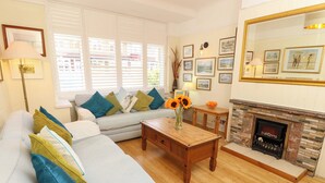 A living room with a sofa, a coffee table, a fireplace, and a wall with framed pictures. - 32 Cranleigh Close (Bournemouth)