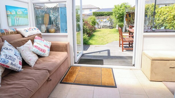 A cozy living room with a brown sofa, cushions, a glass door leading to a garden, and a dining area with a table and chairs. - 32 Cranleigh Close (Bournemouth)