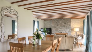 A dining area with a wooden table and chairs, a mirror, and a vase with flowers. - Tyn Towyn - Ty Coch (Holyhead)
