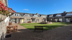 A courtyard with stone buildings, a fountain, and outdoor seating. - Tyn Towyn - Ty Coch (Holyhead)