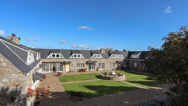 A stone building with multiple windows and a courtyard with a fountain. - Tyn Towyn - Ty Coch (Holyhead)