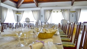 A long dining table set with glassware, plates, and a basket, flanked by striped chairs in a room with wooden beams and curtains. - Parco delle Stelle (Castelmauro)