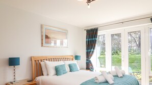 A bedroom with a bed, a nightstand, a lamp, a window with curtains, and a view of the outdoors. - Admiral's Retreat (Weymouth)