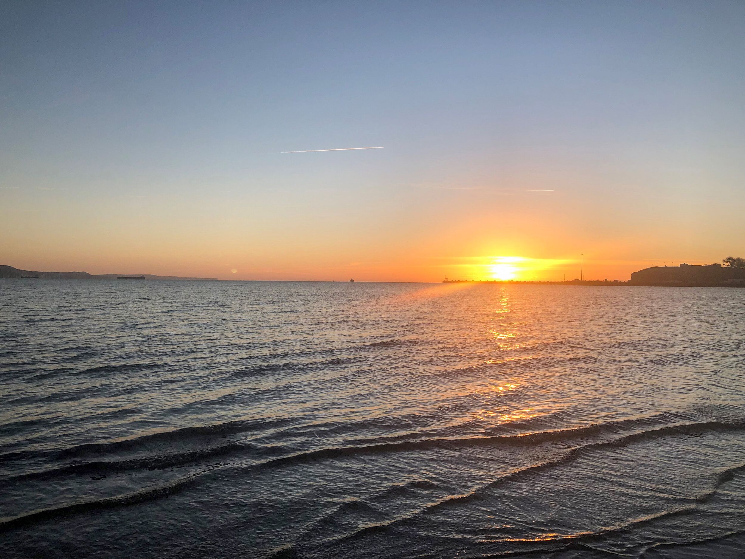 Un coucher de soleil sur une mer calme, avec de douces vagues et une côte lointaine.