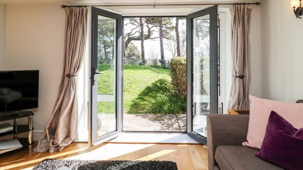 A living room with a TV, a sofa, and a large glass door leading to a garden. - Admiral's Retreat (Weymouth)