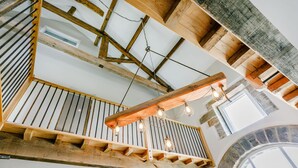 A wooden staircase with a railing, a wooden ceiling with exposed beams, and a stone archway. - Top Barn (Sowerby Bridge)