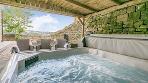 A hot tub with wicker chairs and a stone wall backdrop. - Top Barn (Sowerby Bridge)