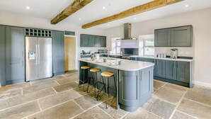 A modern kitchen with a central island, bar stools, and a large refrigerator. - Top Barn (Sowerby Bridge)
