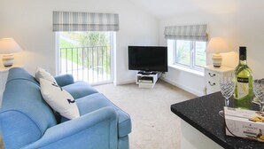 A modern living room with a blue sofa, a flat-screen TV, and a dining area with a black countertop. - Amolca (Amlwch)