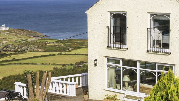 A coastal house with a balcony, a view of the sea, and a lighthouse in the distance. - Amolca (Amlwch)