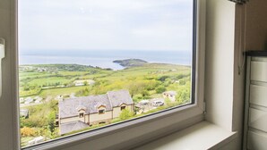 A window with a view of a coastal landscape, including houses and a lighthouse. - Amolca (Amlwch)