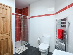 A bathroom with a glass shower enclosure, a white toilet, and a towel rack with a red towel. - Cennin (Criccieth)