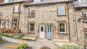 A stone-built row of terraced houses with multiple windows, a blue door, and a small garden with flowers. - Wyebrow Cottage (Bakewell)