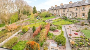 A residential area with stone houses, a garden with various plants, and a clear sky. - Wyebrow Cottage (Bakewell)