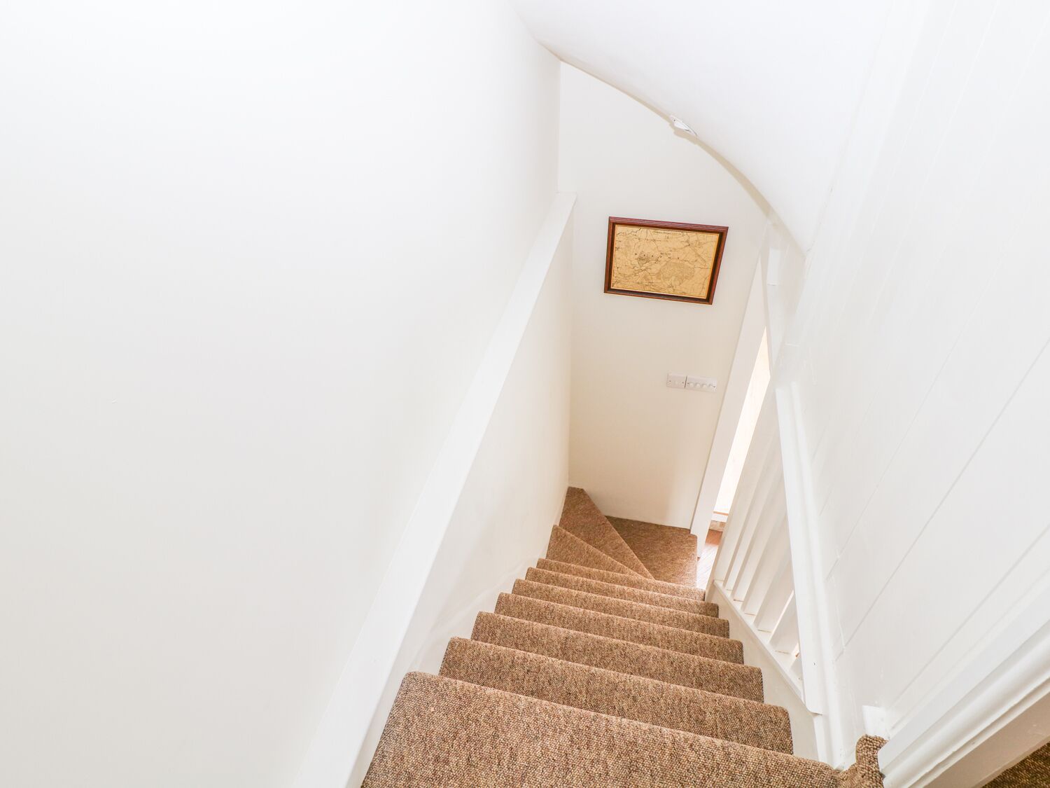 A staircase with carpeted steps leading up to a landing with a framed picture on the wall.