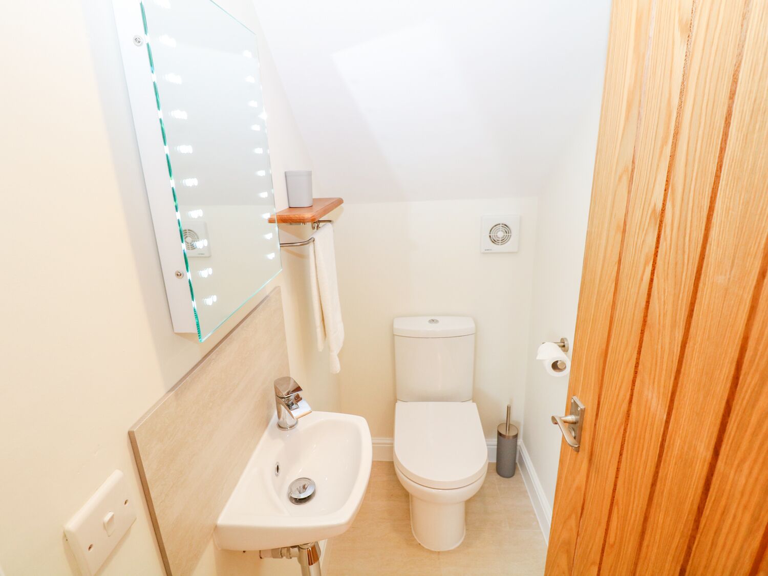 A small bathroom with a sink, toilet, and mirror with lights.