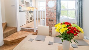 A modern kitchen with white cabinets, a brick accent wall, and a dining area with a wooden table and chairs. - Wyebrow Cottage (Bakewell)