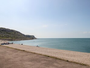 Ein Küstenstrand mit kiesigem Ufer, ruhigem Meer und fernen Klippen.