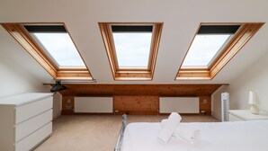 A room with a sloped ceiling, skylights, a bed, a dresser, a radiator, and a lamp. - The View (Portland)