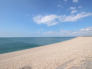 Een breed kiezelstrand met een heldere lucht en een kalme zee.
