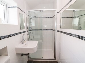 Ein Badezimmer mit einer Glastrennwand zur Dusche, einem weißen Waschbecken und schwarzen Fliesenwänden.