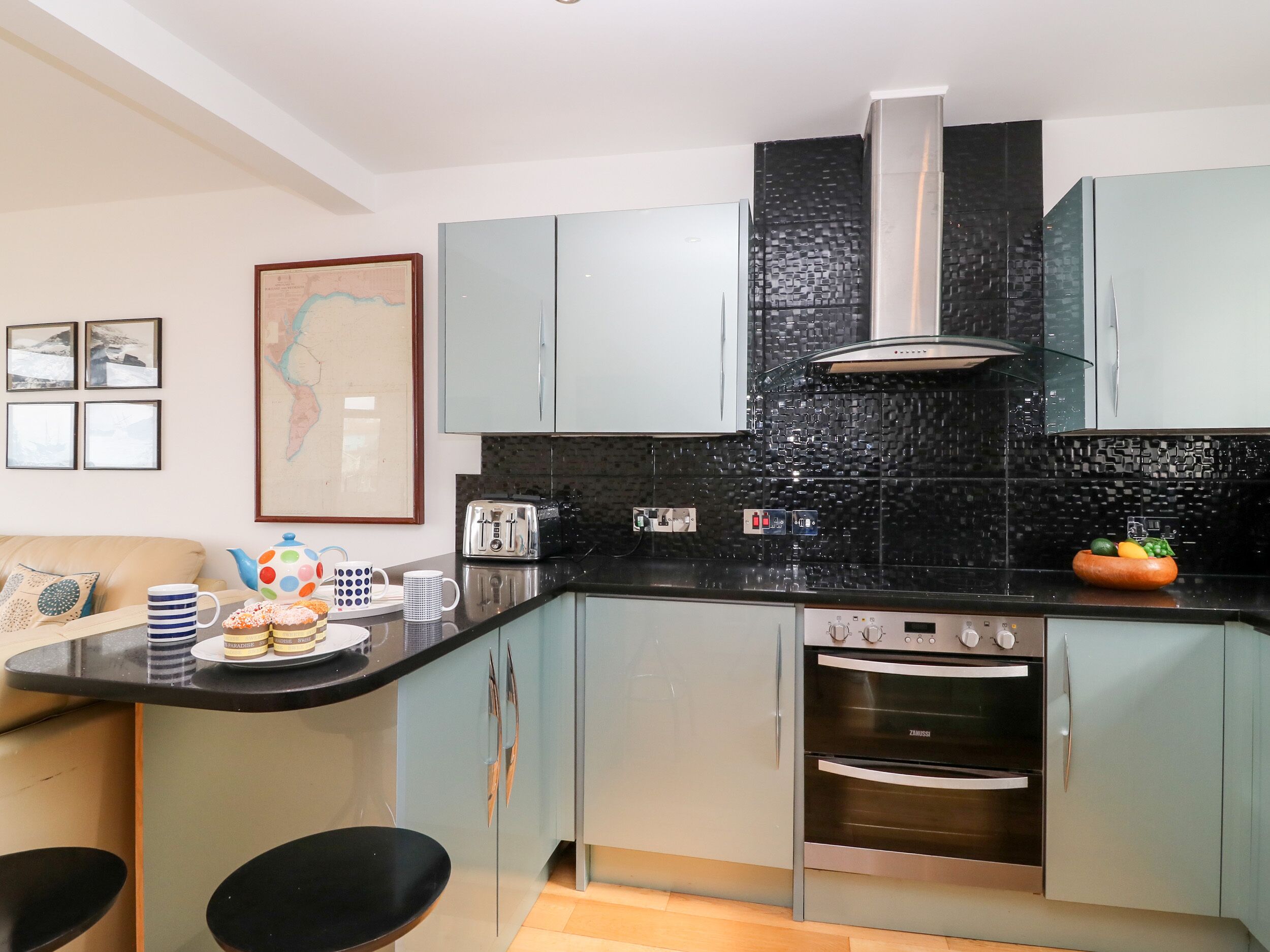 A modern kitchen with light blue cabinets, a black backsplash, and stainless steel appliances including a stove and oven.