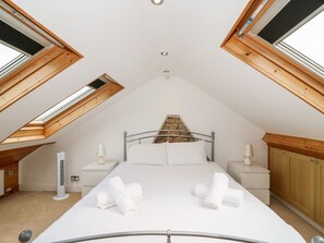 Ein Schlafzimmer mit schrägen Wänden, Dachfenstern, einem Bett mit weißer Bettwäsche, zwei Nachttischen mit Lampen und einem Kleiderschrank.