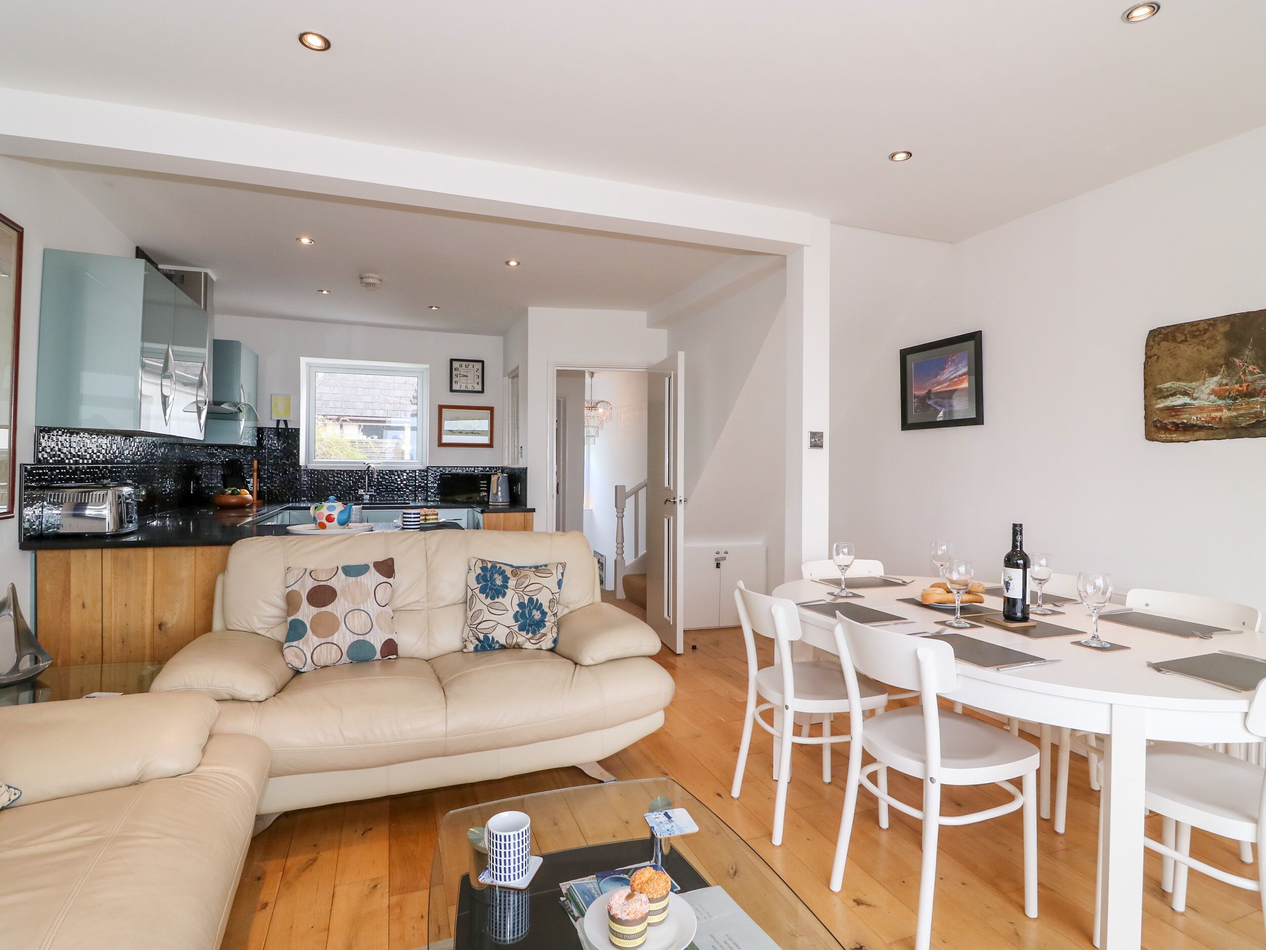 A modern living room with a beige sofa, a glass coffee table, and a dining area with white chairs and a table.