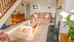 A living room with a wooden staircase, a floral sofa, a coffee table, and a vintage radio. - Kirkstone Cottage (Ambleside)