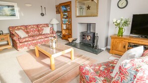 A living room with a sofa, coffee table, fireplace, television, and a bookshelf. - Kirkstone Cottage (Ambleside)